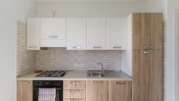 A compact kitchen with white cabinets, a wooden cabinet, a gas stove, a sink, and a tiled backsplash.