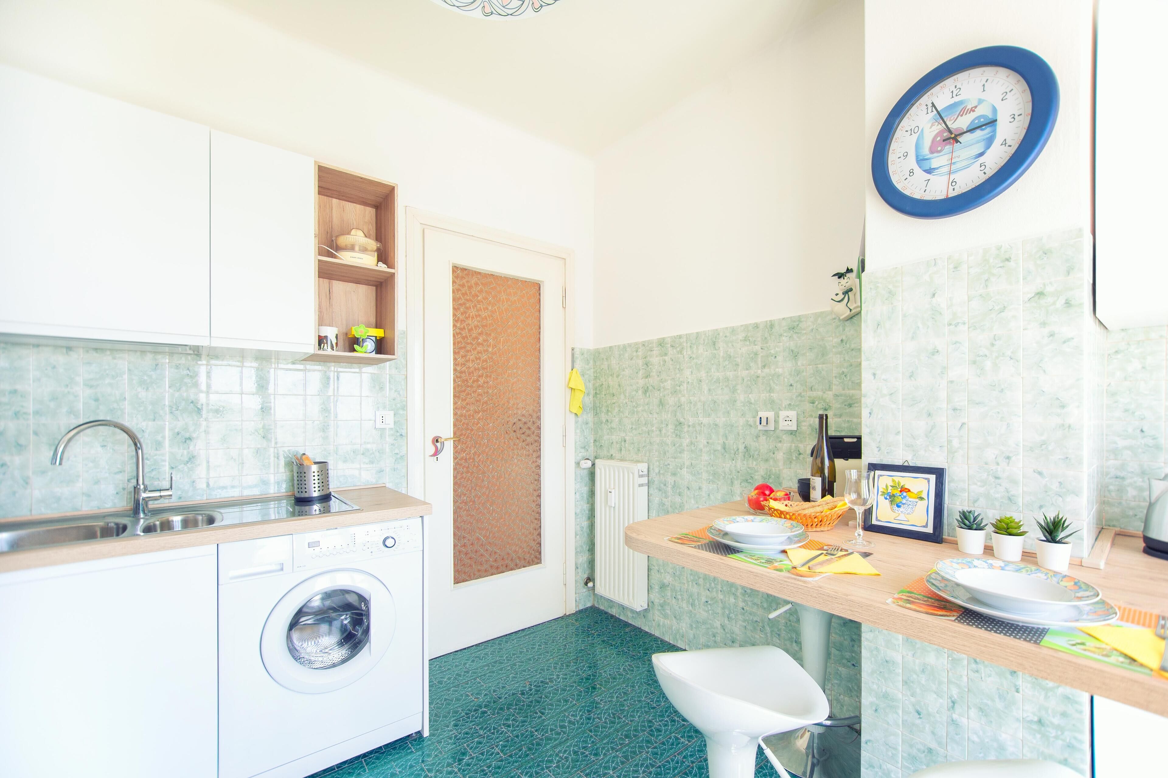 A compact kitchen with a washing machine, sink, and a clock on the wall.