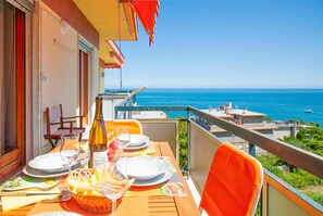 Mesa lista para cenar con vista al mar, una botella de vino y una cesta de pan.
