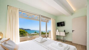A hotel room with a bed, a TV, a minibar, and a balcony with a view of the sea. - Villa Stavroula - Two Bedroom Villa, Sleeps 4 (Mparmpati)