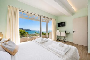 Ein Hotelzimmer mit Bett, Fernseher, Minibar und einem Balkon mit Meerblick.