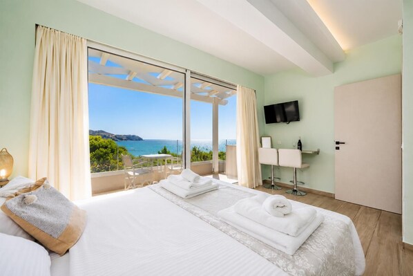 A hotel room with a bed, a TV, a minibar, and a balcony with a view of the sea. - Villa Stavroula - Two Bedroom Villa, Sleeps 4 (Mparmpati)