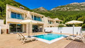 Eine moderne Villa mit Swimmingpool, Sitzgelegenheit im Freien und Blick auf die Berge.