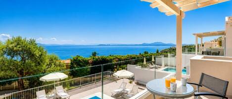 A balcony with a pool, lounge chairs, and a table with drinks.