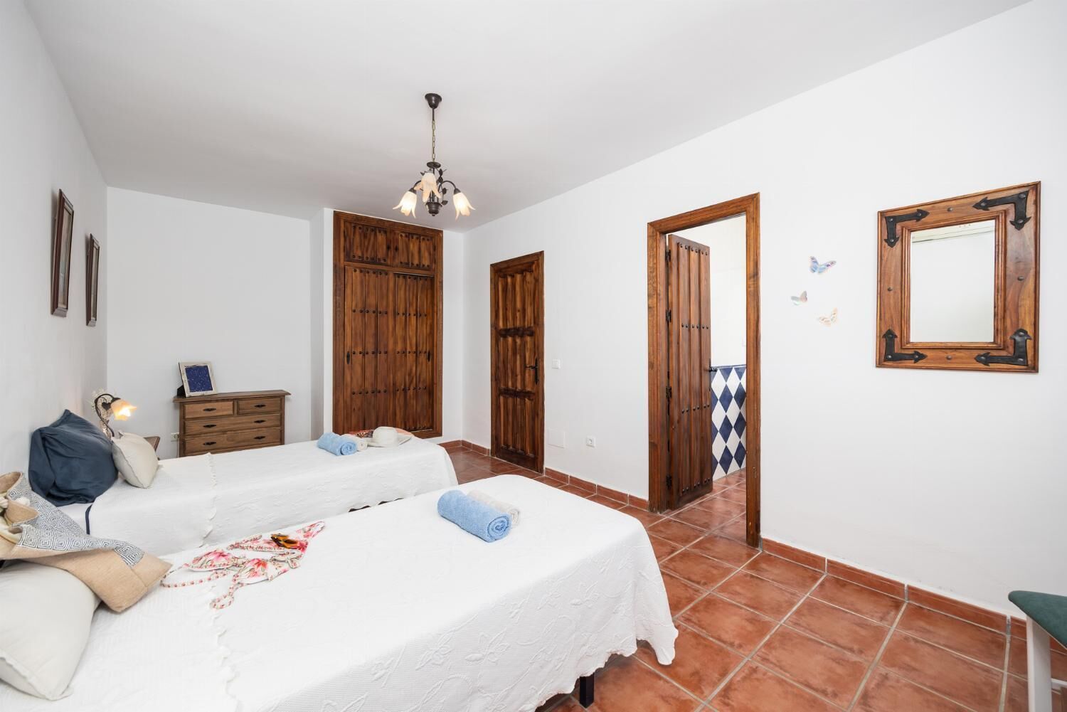 Un dormitorio con dos camas, armarios de madera, un aparador, un espejo y una lámpara colgante.
