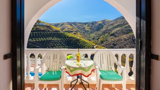 Ein Balkon mit zwei weißen Stühlen und einem Tisch mit Blick auf einen Weinberg.