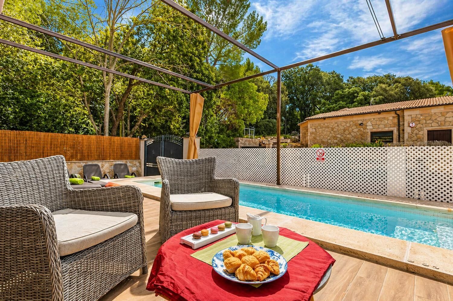 A poolside area with wicker furniture, a table with croissants, and a pool.