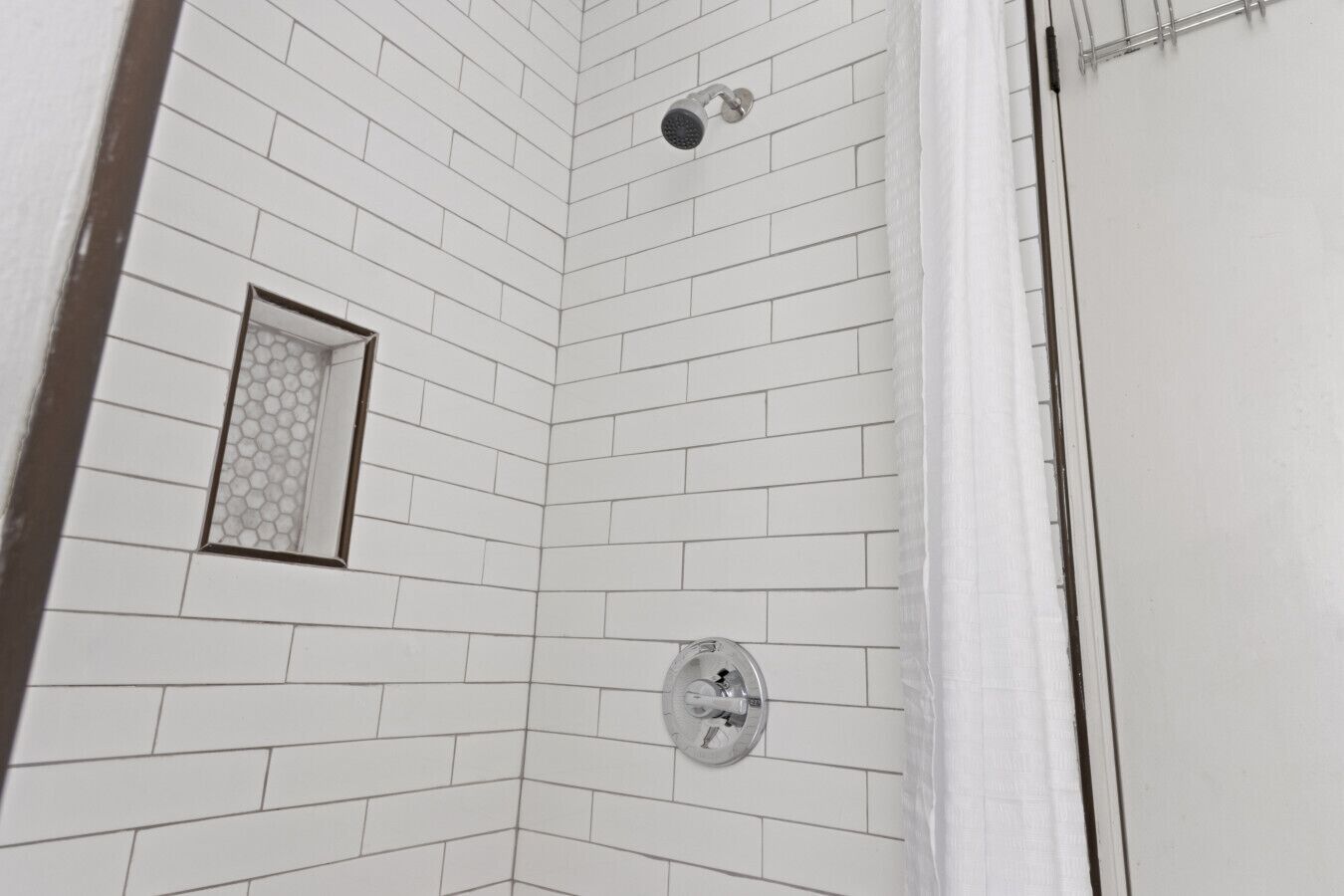 Un coin d’une pièce aux murs recouverts de carreaux blancs et comprenant un espace douche.