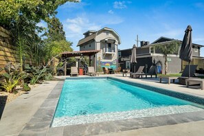 A rectangular swimming pool with a tiled edge, surrounded by lounge chairs and umbrellas, with a building in the background. - Cute and Cozy One Bedroom in Hotel with Shared Pool and Hot tub (New Orleans)
