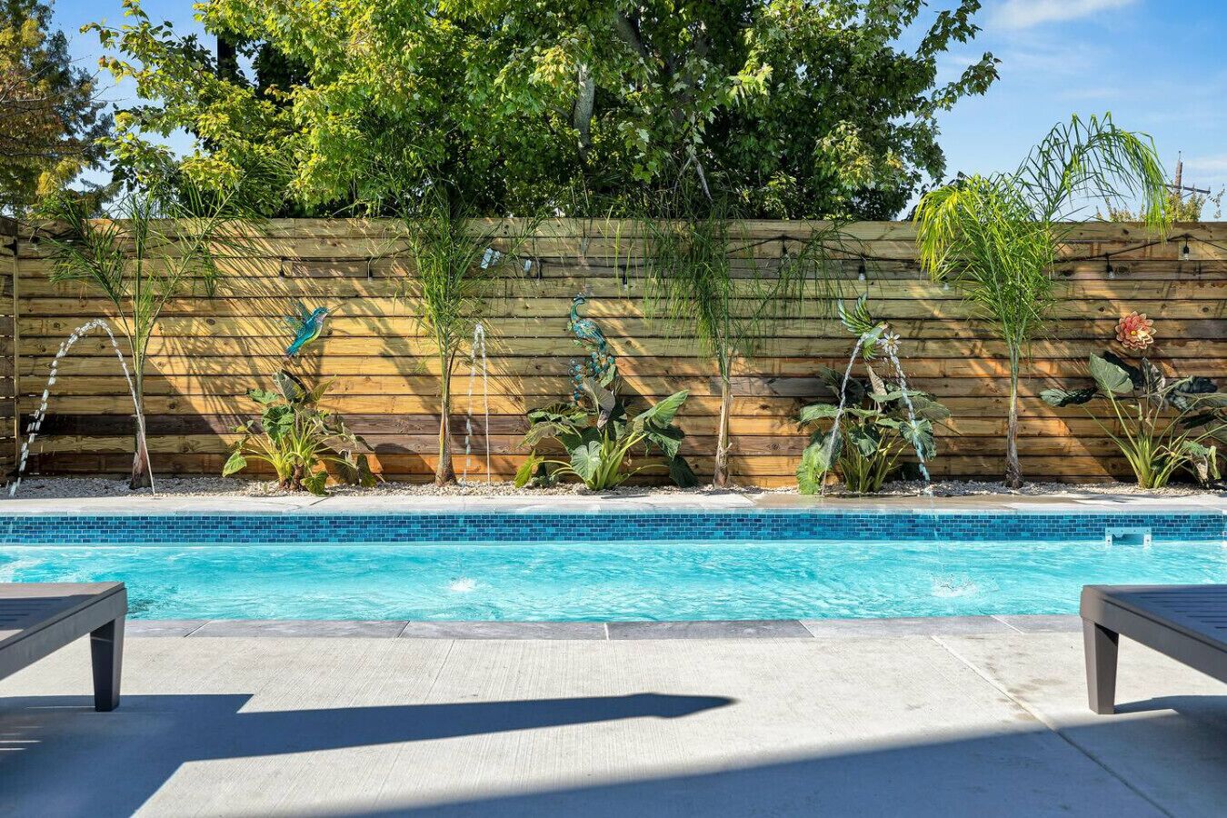Una piscina con cerramiento de madera y plantas tropicales.
