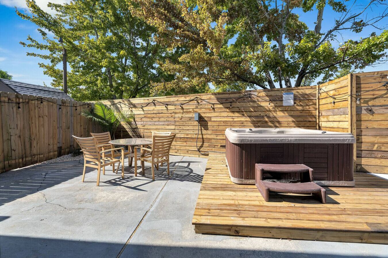 An outdoor patio with a hot tub, wooden deck, and a table with chairs.