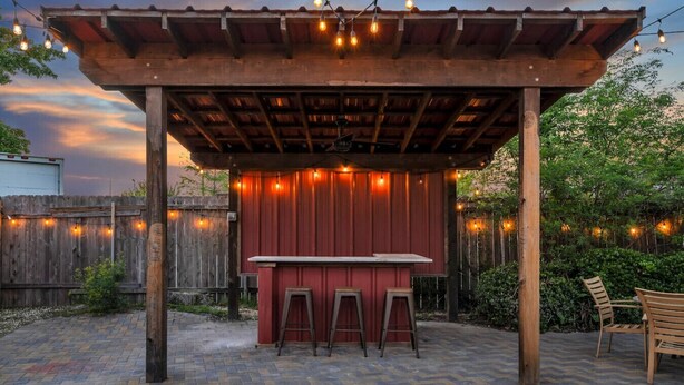 A covered outdoor bar area with a red wall, wooden stools, and string lights. - Cute and Cozy One Bedroom in Hotel with Shared Pool and Hot tub (New Orleans)