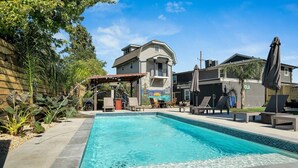 A rectangular swimming pool with a tiled edge, surrounded by lounge chairs and umbrellas, with a building in the background. - Cute and Cozy One Bedroom in Hotel with Shared Pool and Hot tub (New Orleans)