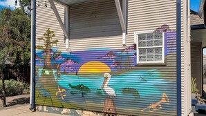 A house with a colorful mural on the garage door depicting a sunset scene with a pelican, a boat, and a whale. - Cute and Cozy One Bedroom in Hotel with Shared Pool and Hot tub (New Orleans)