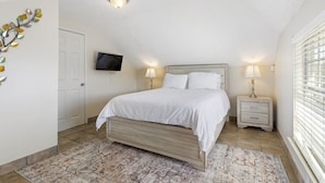 A bedroom with a bed, two bedside tables, a TV, and a patterned rug. - Cute and Cozy One Bedroom in Hotel with Shared Pool and Hot tub (New Orleans)