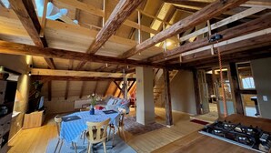 Ein rustikales Holzinterieur mit hohen Decken, einem Essbereich mit Tisch und Stühlen sowie einer sichtbaren Küchenzeile mit Herd.