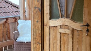 Eine Holztür mit Fensterglas, ein Korbstuhl mit weißem Kissen und ein fliesenbelagter Eingangsbereich.