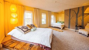 A bedroom with a large bed, a smaller bed, and a bench. There are windows, curtains, and a wall with tree silhouettes. - DV-627 Walk to Breweries! Pets OK! (Davis)