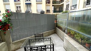 Een terras buiten met een tafel en stoelen met een glazen blad, omringd door een hoge muur en potplanten.