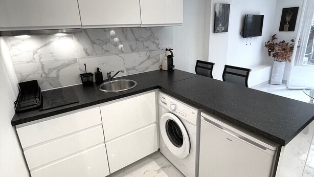 Een moderne keuken met witte kastjes, een marmeren achterwand, een ingebouwde wasmachine en een zwart aanrecht.