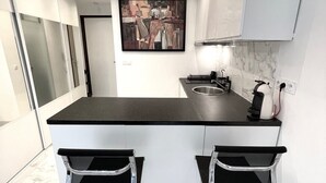 Een moderne keuken met een marmeren aanrechtblad, twee barkrukken en een schilderij boven de spoelbak.