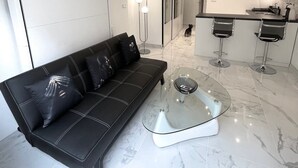 Een moderne woonkamer met een leren bank, een glazen salontafel en een keuken op de achtergrond.