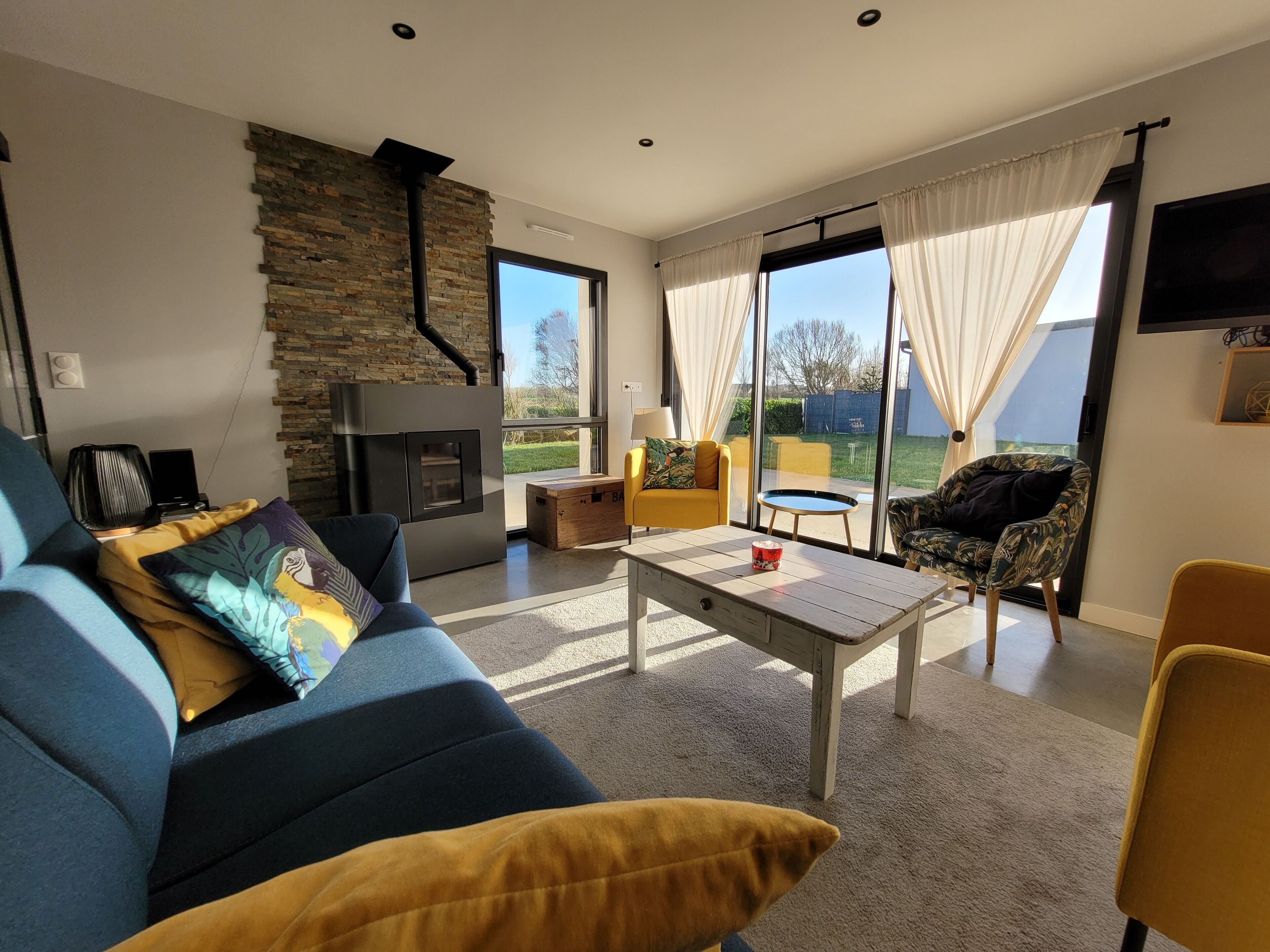 A modern living room with a stone fireplace, a sofa, a coffee table, and a view of the outdoors through large windows.