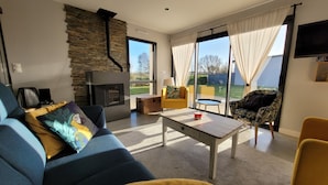 Un salon moderne avec une cheminée en pierre, un canapé, une table basse et une vue sur l’extérieur grâce à de grandes fenêtres.