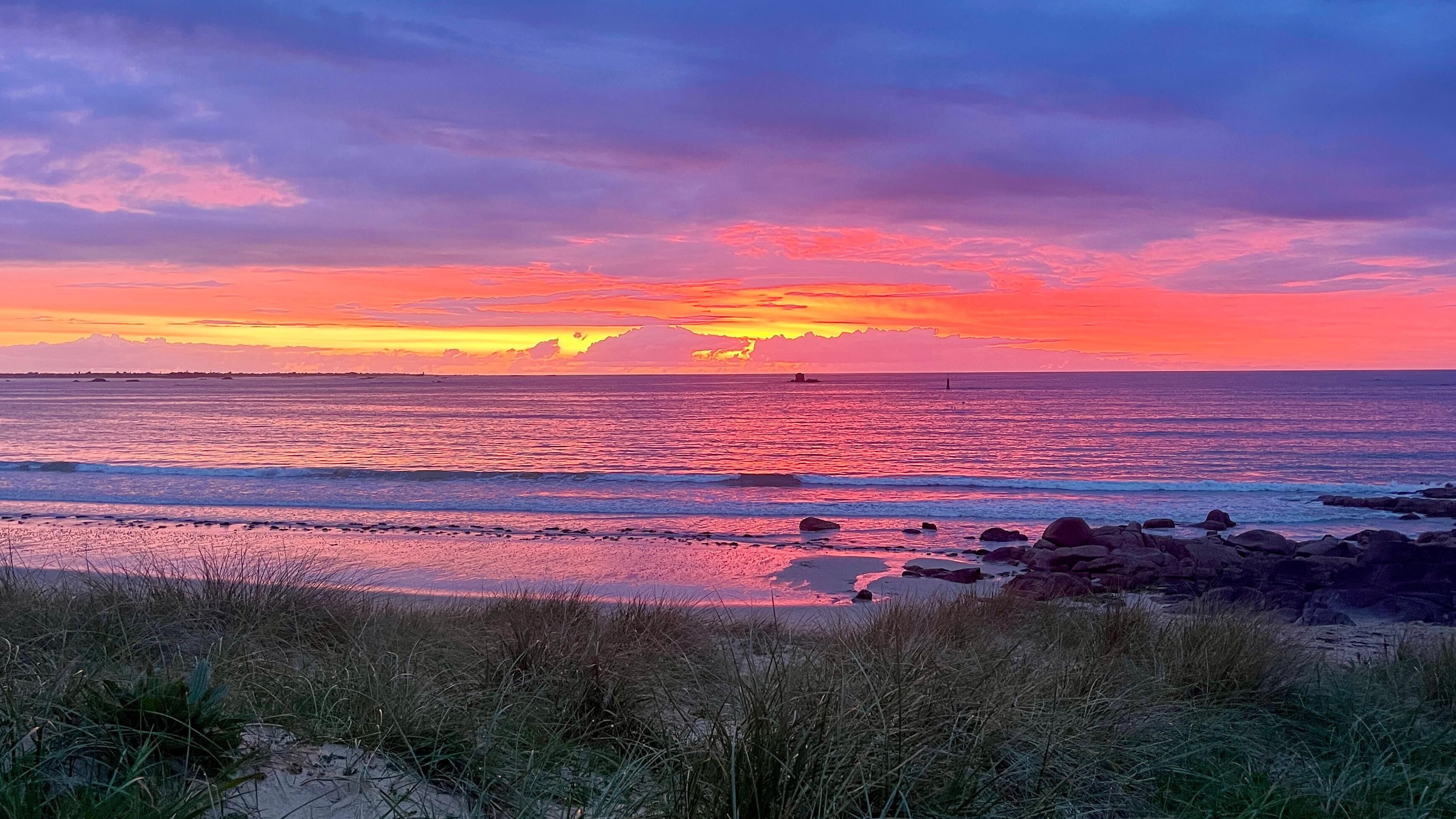 Una playa con atardecer, olas y rocas.