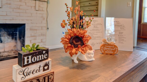 Een houten toonbank met een bloemstuk, een beeldje van een witte kat en houten borden met tekst.