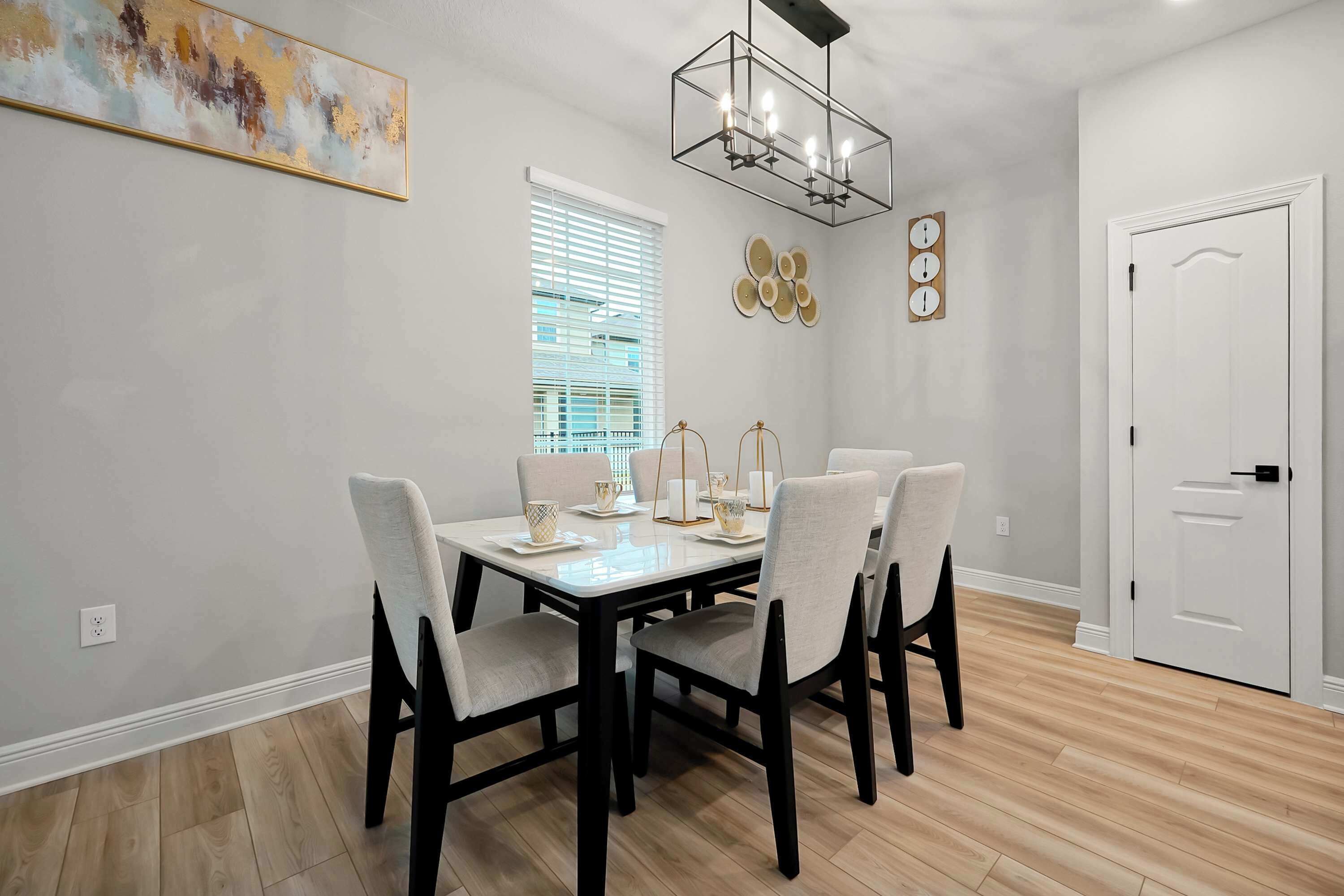 Un comedor con una mesa rectangular, cuatro sillas, una araña y una ventana con persianas.