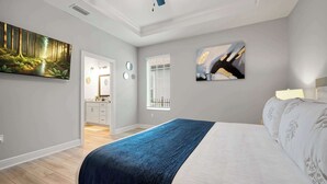 Een slaapkamer met een bed, een schilderij van een bos, een raam met zonwering en een badkamer zichtbaar door een open deur.