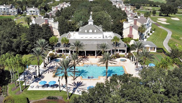 Een groot resort met een centraal gelegen zwembad, omringd door palmbomen en een golfbaan op de achtergrond.