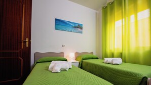 A hotel room with two beds, green bedding, a painting of a beach, a nightstand with a lamp, and a wooden door. - VILLA HEMINGWAY - ALESSIA'S HOUSE BREATHTAKING SEA VIEW (Ficarazzi)