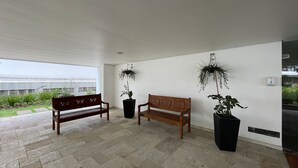 Un espacio interior amplio con dos bancos de madera y plantas grandes en macetas.
