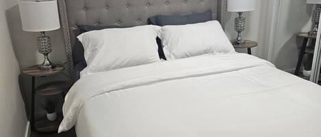 A neatly made bed with white linens, a tufted headboard, and two bedside lamps.