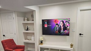 En moderne stue med et fladskærms-tv monteret på væggen, en rød lænestol, en turkis sofa og et hvidt tv-møbel.