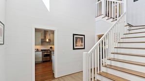 A modern interior with a staircase, wooden flooring, and a kitchen visible through an open doorway. - Hope Cottage sleeps 8 with a heated pool (St Simons Island)