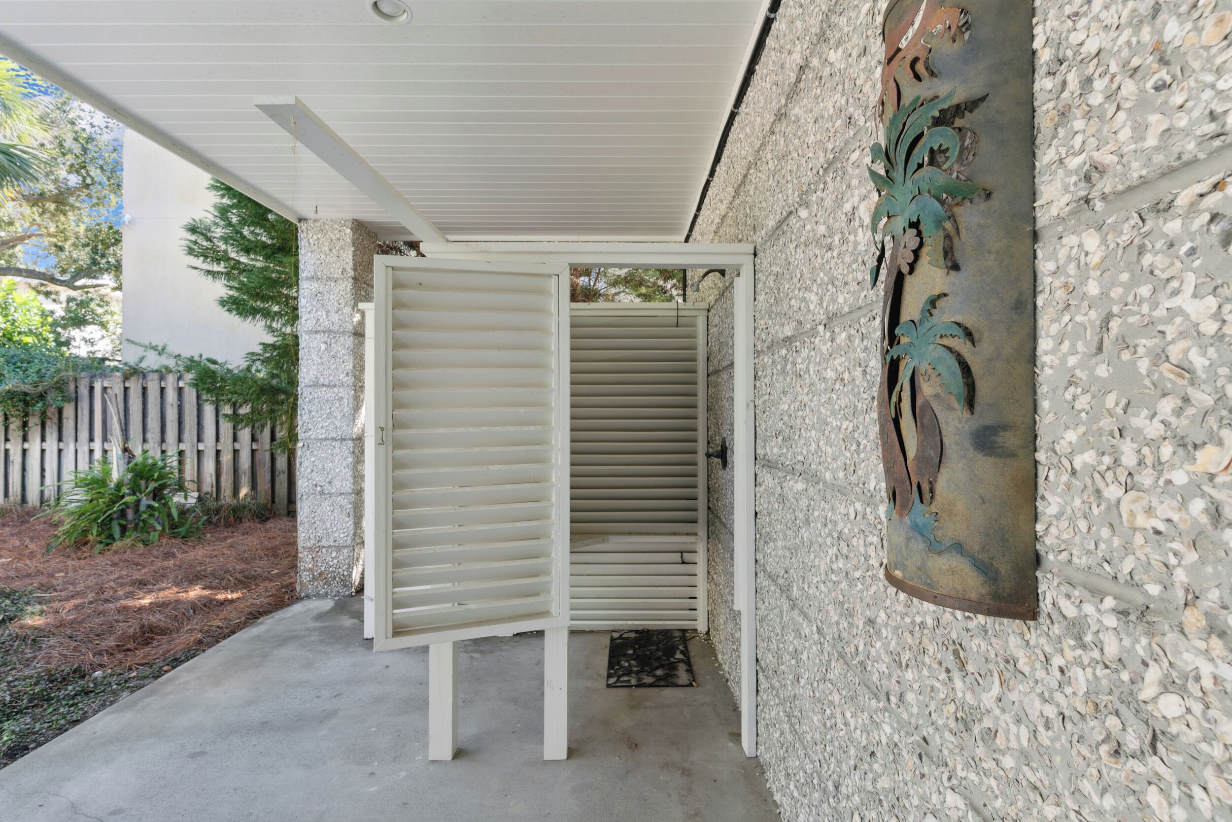 Un espace extérieur abrité, doté d’une porte blanche, d’un mur en pierre orné de sculptures et d’un sol en béton.
