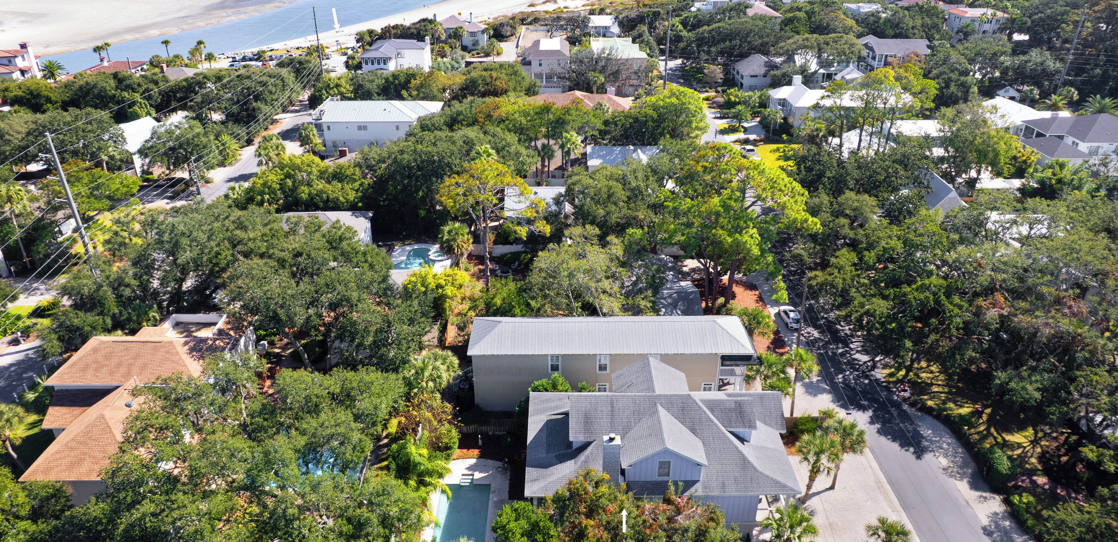 An aerial view of a residential area with houses, trees, and a beach in the background.