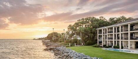 A beachfront hotel with a pool, a rocky shoreline, and a sunset view.