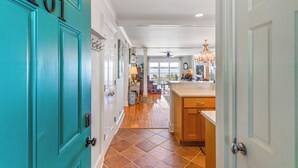 A hallway leading to a kitchen with teal doors, wooden flooring, and a chandelier. - Ocean Front Escape sleeps 4 (St Simons Island)