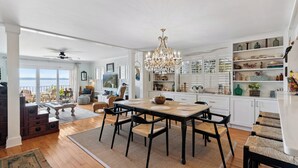 A spacious dining area with a large wooden table and black chairs, a chandelier, and a view of the sea through large windows. - Ocean Front Escape sleeps 4 (St Simons Island)