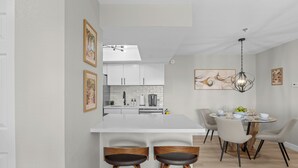 A modern kitchen with white cabinets, a central island, and bar stools. There is a dining area with a round table and chairs. - Modern Las Vegas Condo Near Strip w/ Pool & Gym and free parking NO RESORT FEES (Paradise)