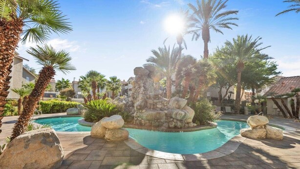 A swimming pool with a rock waterfall feature, surrounded by palm trees and a stone pathway. - Modern Las Vegas Condo Near Strip w/ Pool & Gym and free parking NO RESORT FEES (Paradise)