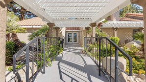 A covered walkway leading to a building with a door, surrounded by greenery and palm trees. - Modern Las Vegas Condo Near Strip w/ Pool & Gym and free parking NO RESORT FEES (Paradise)