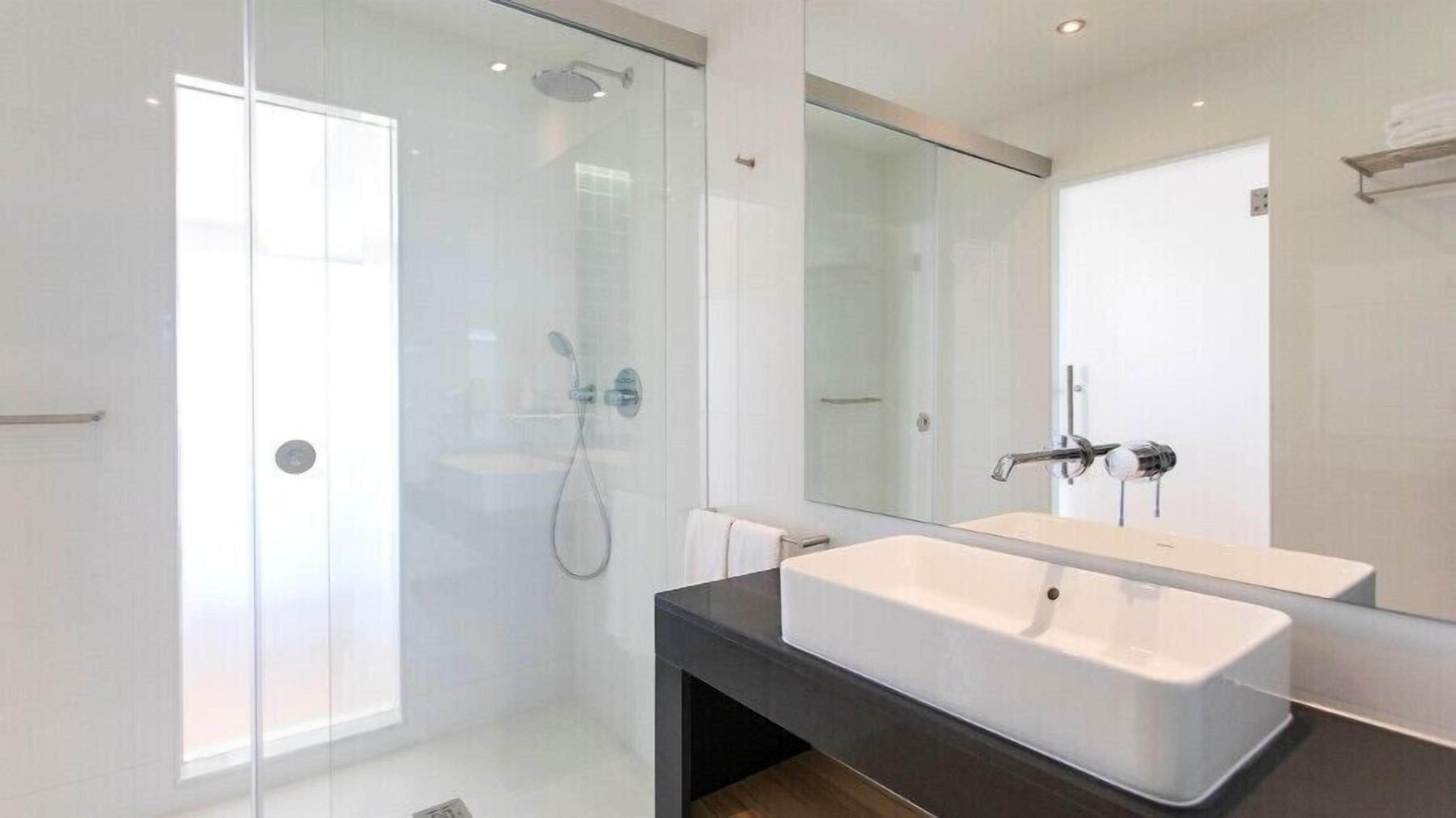 Un baño moderno con cabina de ducha de vidrio, un espejo grande y encimera oscura.