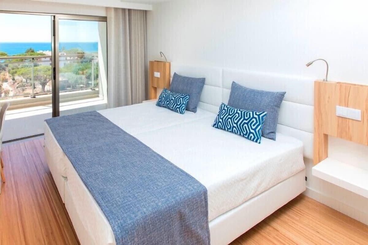 Habitación de hotel con cama, escritorio, silla, lámpara y vista al océano.