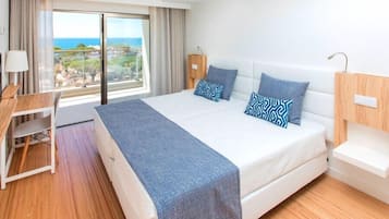 Une chambre d’hôtel avec un lit, un bureau, une chaise, une lampe et une vue sur l’océan.