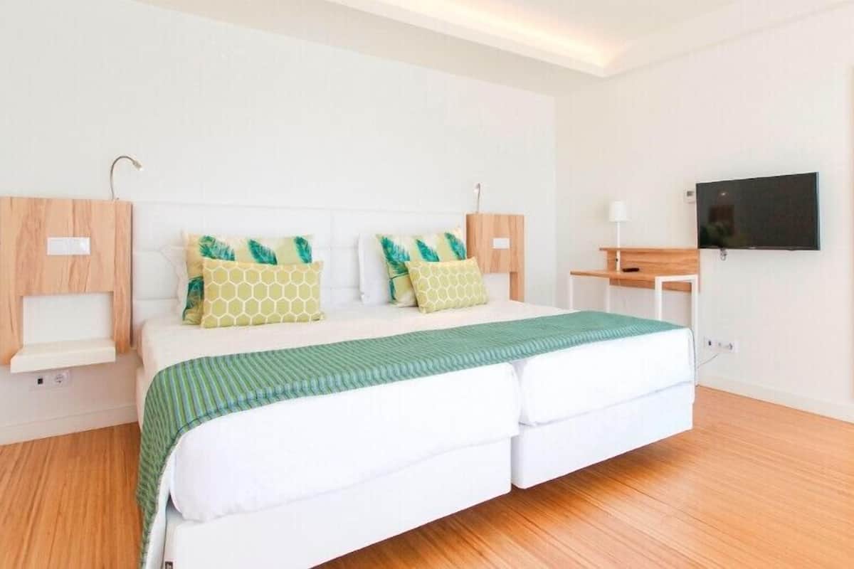 Un dormitorio moderno con cama, televisor, espejo y un pequeño escritorio.